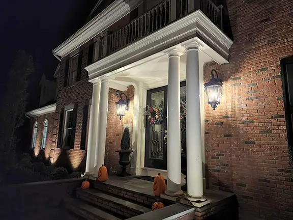 Professional brick entryway with sconces and column uplighting at night