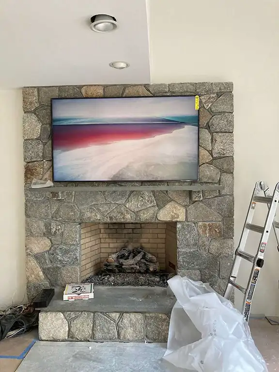Mounted TV installation above stone fireplace with recessed lighting